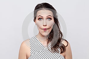 Portrait of funny crazy beautiful young brunette woman with makeup and striped dress standing and looking at camera with big eyes