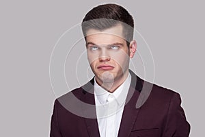 Portrait of funny crazy handsome young man in violet suit and white shirt, standing, looking with crossed eyes and foolish face.