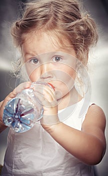 Portrait of a funny cute little girl in a casual dress, drink water while sitting in studio.