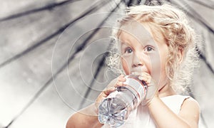 Portrait of a funny cute little girl in a casual dress, drink water while sitting in studio.