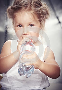 Portrait of a funny cute little girl in a casual dress, drink water while sitting in studio.