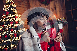 Portrait of funny cute young guy blowing mug sweet cappuccino coffee at home he covered himself warm blanket waiting