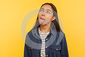 Portrait of funny dumb crazy girl in denim shirt showing tongue out and looking cross-eyed with silly brainless expression