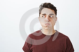 Portrait of funny european male model in red t-shirt, holding breat, sulking and looking left while holding water in