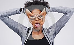 Portrait, funny face and finger glasses with an african woman in studio on a gray background looking silly or goofy
