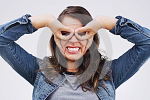 Portrait, funny face and finger glasses with a woman in studio on a white background looking silly or goofy. Comedy