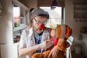 Portrait of funny female doctor with red clown nose holding teddy bear.