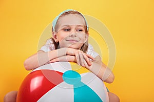 Portrait of funny happy child in summer clothes with beachball on yellow background