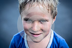 Portrait of a funny happy mischievous cheerful cute blond blue eyed boy making freckles dirty face while playing