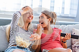 Portrait of funny and happy young women watching comedy in bed and laughing. Cheerful friends eating tasty popcorn and looking