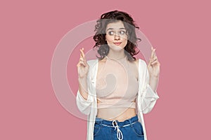 Portrait of funny hopeful beautiful brunette young woman with curly hairstyle in casual style standing with crossed finger and