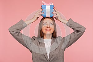 Portrait of funny joyful businesswoman in suit jacket holding present on head and smiling, celebrating anniversary photo