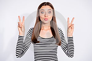 Portrait of funny lady sending air kisses making v-signs wearing striped sweater  over white background