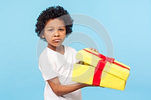 Portrait of funny little boy holding unpacked gift box and looking at camera with upset dissatisfied grimace