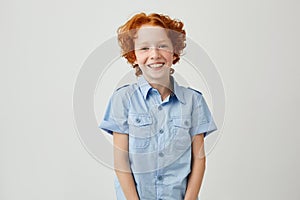 Portrait of funny little boy with red hair and freckles smiling brightfully, looking in camera, posing for family photo