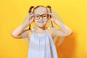 Portrait of a funny little girl on a yellow background. Preschool child straightens glasses