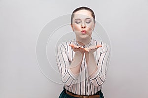 Portrait of funny in love beautiful young woman in striped shirt and makeup and collected ban hairstyle, standing with closed eyes