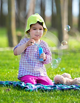 Portrait of funny lovely little girl blowing soap bubbles in the park