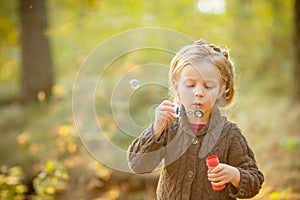 Portrait of funny lovely little girl blowing soap bubbles.Cute blonde blue-eyed girl in yellow knitted coat in the