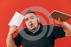 Portrait of a funny man with a beard and overweight with a notebook and a book in his hands on a red background