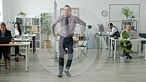 Portrait of funny man dancing in office while businesspeople working in background