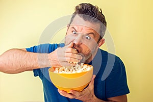 Portrait of a funny man eating popcorn isolated over yellow background