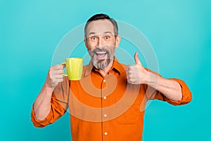 Portrait of funny middle age brunet hair businessman wear orange shirt thumb up rate tasty holding coffee isolated on