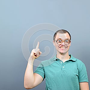 Portrait of funny nerd with big eyes having an idea  and showing at empty space above against gray background