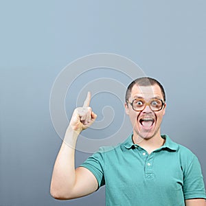 Portrait of funny nerd guy having an idea  and showing at empty space above against gray background