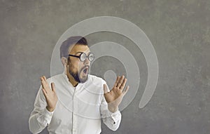 Portrait of funny nerd man in glasses with surprised facial expression on gray background.