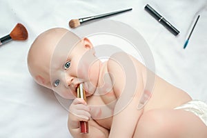 Portrait of a funny newborn baby with red lipstick kisses on the skin with scattered makeup tools on white background. top view