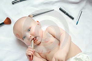 Portrait of a funny newborn baby with red lipstick kisses on the skin with scattered makeup tools on white background. top view