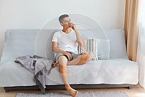 Portrait of funny pensive handsome young adult man wearing white shirt and jeans short, looking away with thoughtful facial