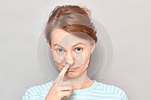 Portrait of funny puzzled girl with white drops of face cream on skin
