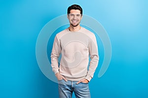 Portrait of funny satisfied man with brunet hairstyle dressed beige sweatshirt standing arms in pockets isolated on blue