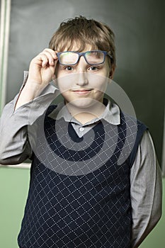 Portrait of a funny schoolboy in glasses at the blackboard