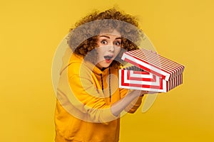 Portrait of funny, shocked curly-haired woman in hoodie looking at camera with amazed expression photo