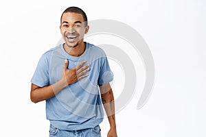 Portrait of funny smiling guy touches his chest, laughing, chuckle over smth hilarious, stands over white background