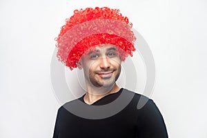 Portrait of funny stylish hipster man with curly red wig smiling at camera, looking playful positive. white background