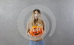 Portrait of funny surprised and little scared teen girl standing with pumpkin in her hands.