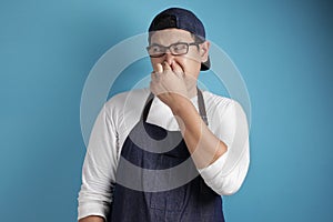 Portrait of funny young male Asian chef or waiter closing his nose, smells something bad