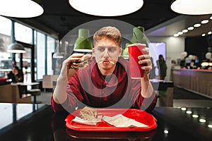 Portrait of a funny young man eating fast food at the background of the restaurant