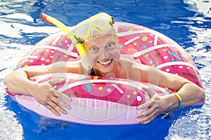 Portrait of a funny young man in swim goggles and inflatable ring having fun in swimming pool