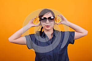 Portrait of funny young woman holding juicy oranges in studio over yellow background