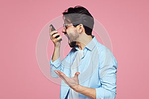 Portrait of a furious young businessman yelling at mobile phone isolated over pink background.