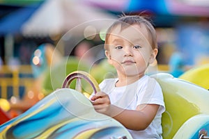 Portrait of future racing champion: toddler child sitting on little bright car on merry-go-round in theme park with proud face