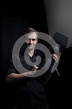 Portrait of a gaffer man with a professional lighting head device in his hands on a black background