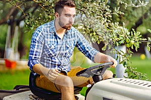 Portrait of gardener using a lawn mowing tractor for cutting grass.