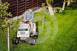 Portrait of gardener using lawn tractor for mowing grass in household garden