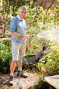 Portrait of gardener watering plants from hose at garden